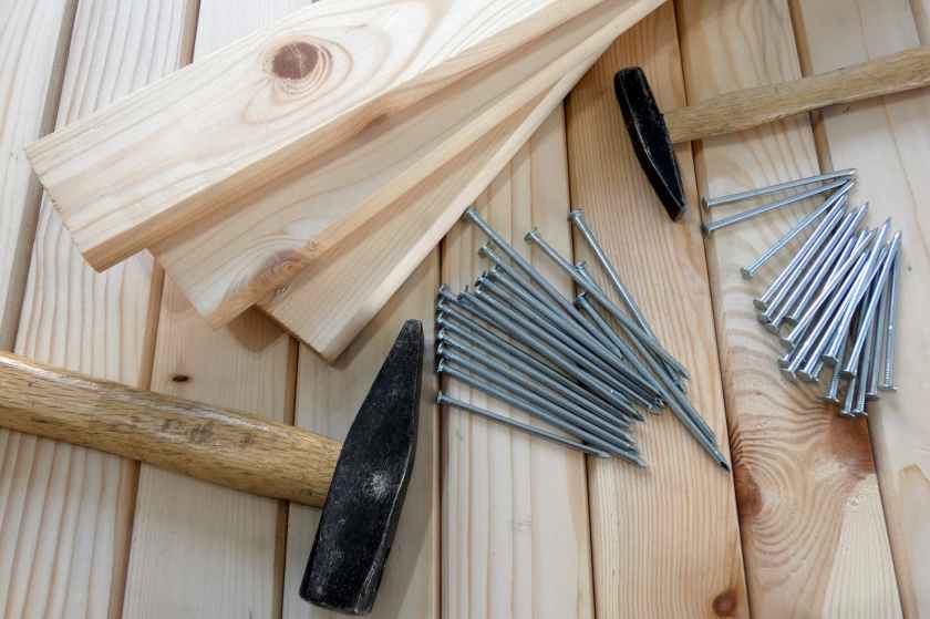 gray nails beside beige wooden planks and hammers